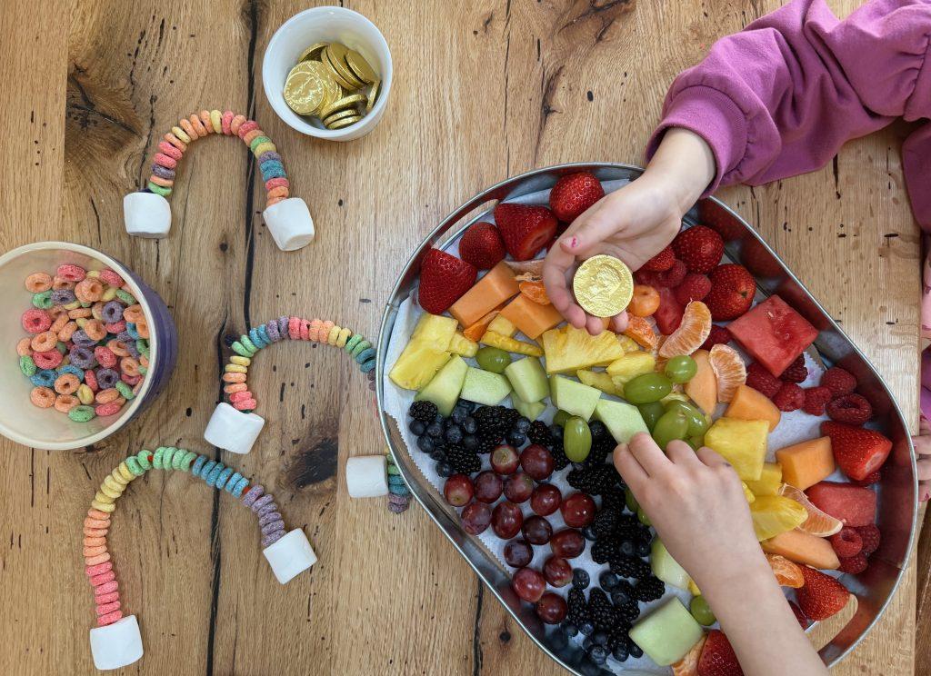 Children's hands over rainbow fruit platter.